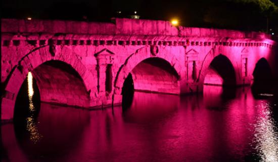 Ponte antico illuminato di rosa, riflesso sull'acqua.